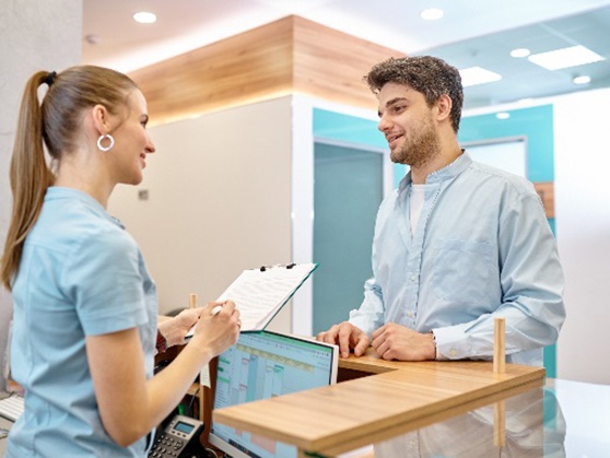 Patient smiling at dental receptionist while paying for treatment