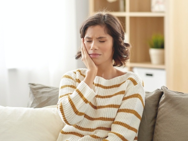 Woman wincing and holding cheek before emergency dentistry