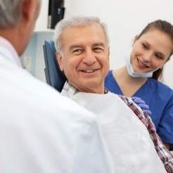 Older man in dental chair smiling at dentist