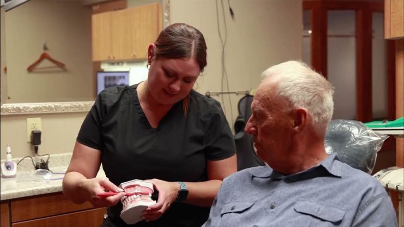 Dental team member showing a denture to a senior man in the dental chair