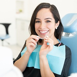 Young woman smiling while holding Invisalign aligners