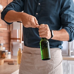 Man using bottle cap opener to remove bottle cap in kitchen