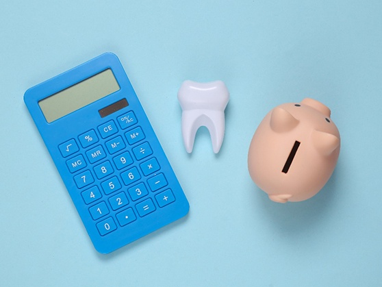 A piggy bank, fake tooth, and calculator against a blue background