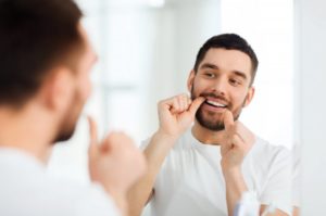 Handsome man flossing in front of bathroom mirror